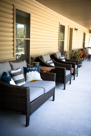 Front Porch Covered Patio Sitting Area with Padded Furniture and Wood Tables, Fragrant 4 o'clocks growing nearby